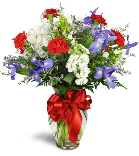 Spirit of Summer™. An arrangement by Avenue Flowers and Gifts. Red carnations, white stock blooms, and blue irises are arranged in a glass vase...